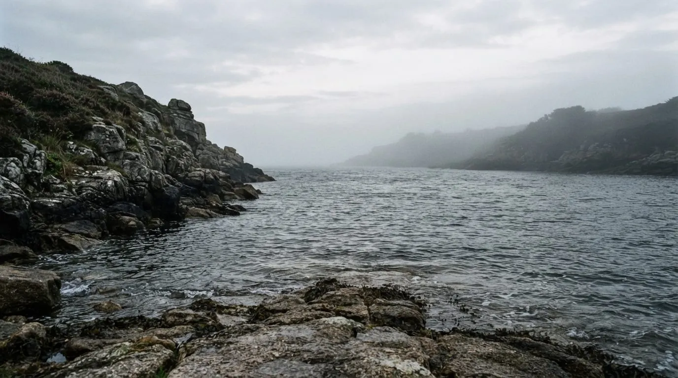 Le bras de mer entre deux côtes rocheuses, la rive opposée visible dans la brume de fin de journée.