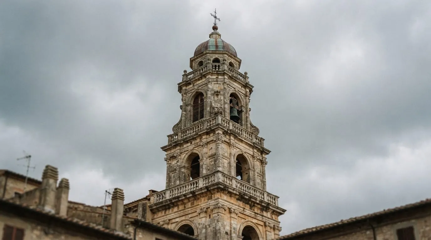 Un campanile baroque en pierre claire à plusieurs étages d’arcades, vu de trois quarts contre un ciel gris