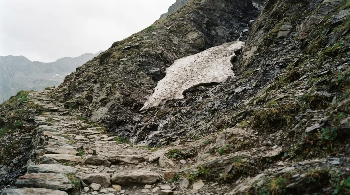 Un névé résiduel accroché dans un couloir orienté nord, au-dessus d'un sentier de pierres sèches, début juin